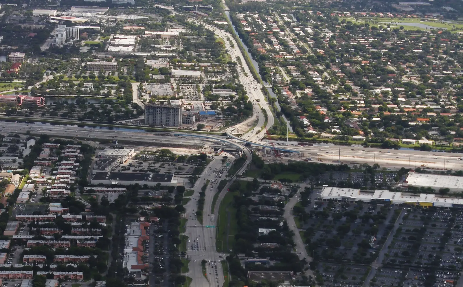 A mid-rise building under construction beside I-595 in Plantation, with University Drive curving north, seen from the air.