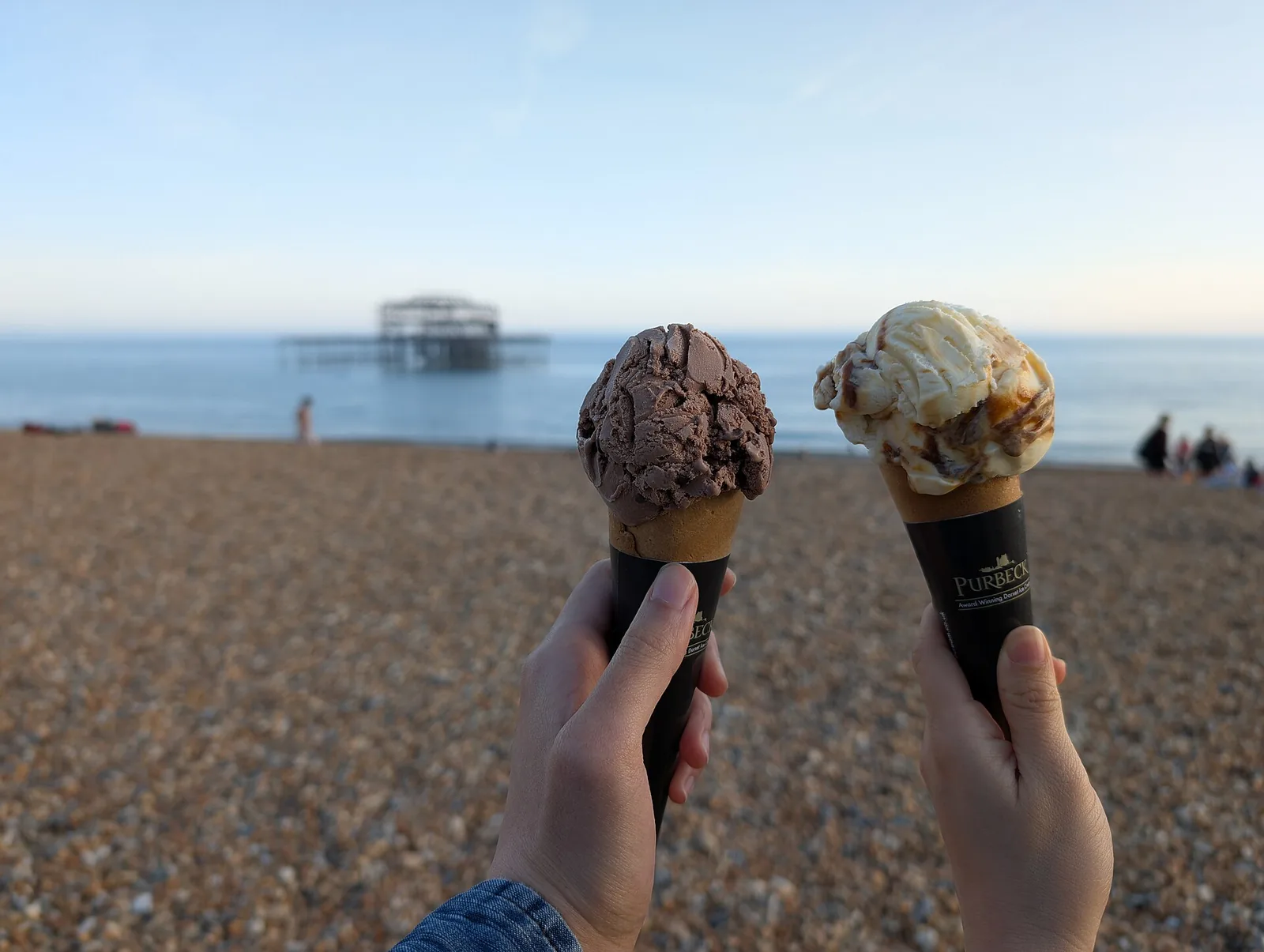 Two ice cream cones held up outdoors.
