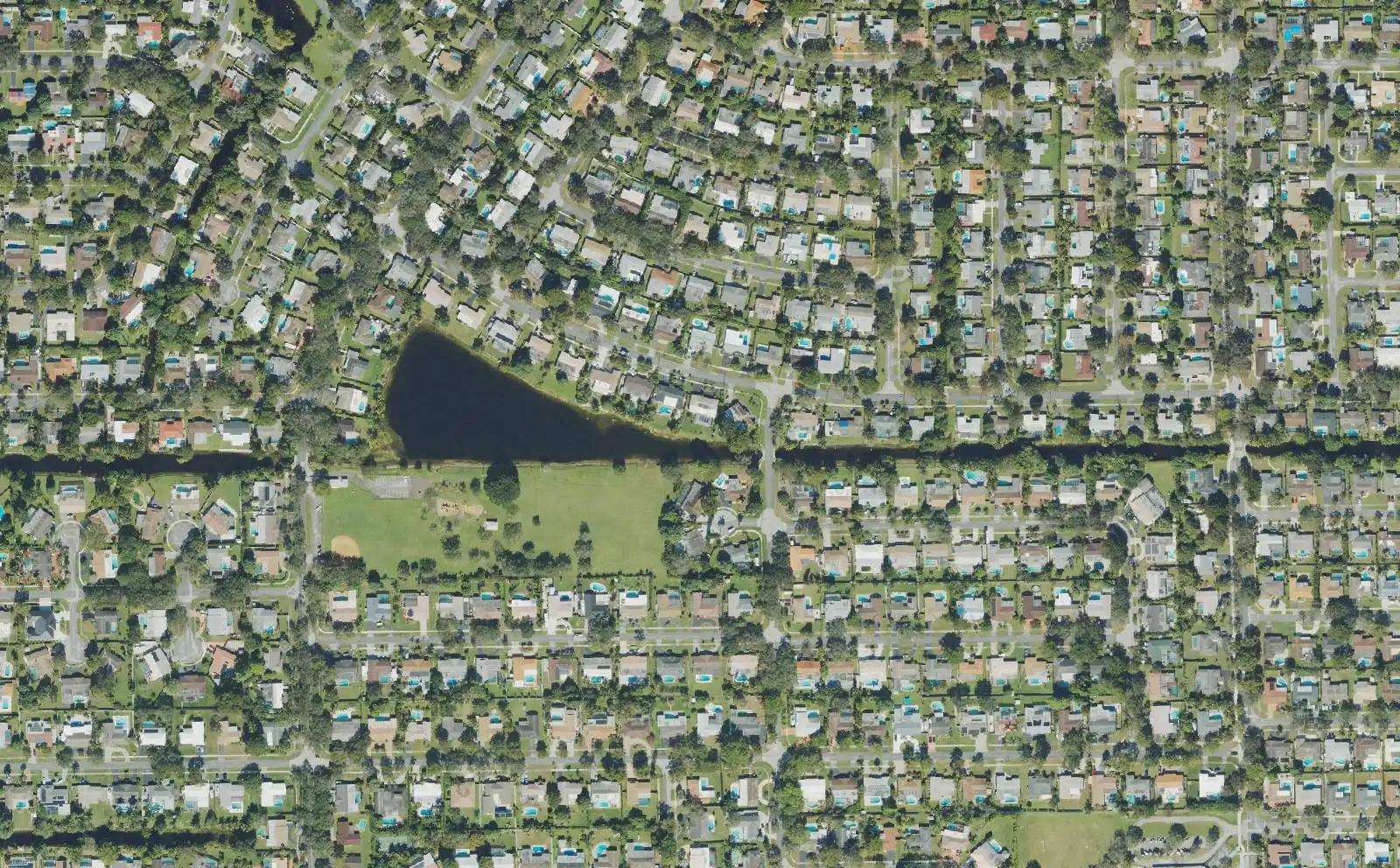 Tree-lined streets of Plantation Park from above, with a lake and an open field in the middle of the neighborhood.